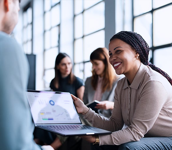 SMiling woman with braids shows a colleague a data report on a laptop screen