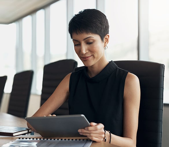 A businesswoman sits in a conference room reviewing data on a tablet